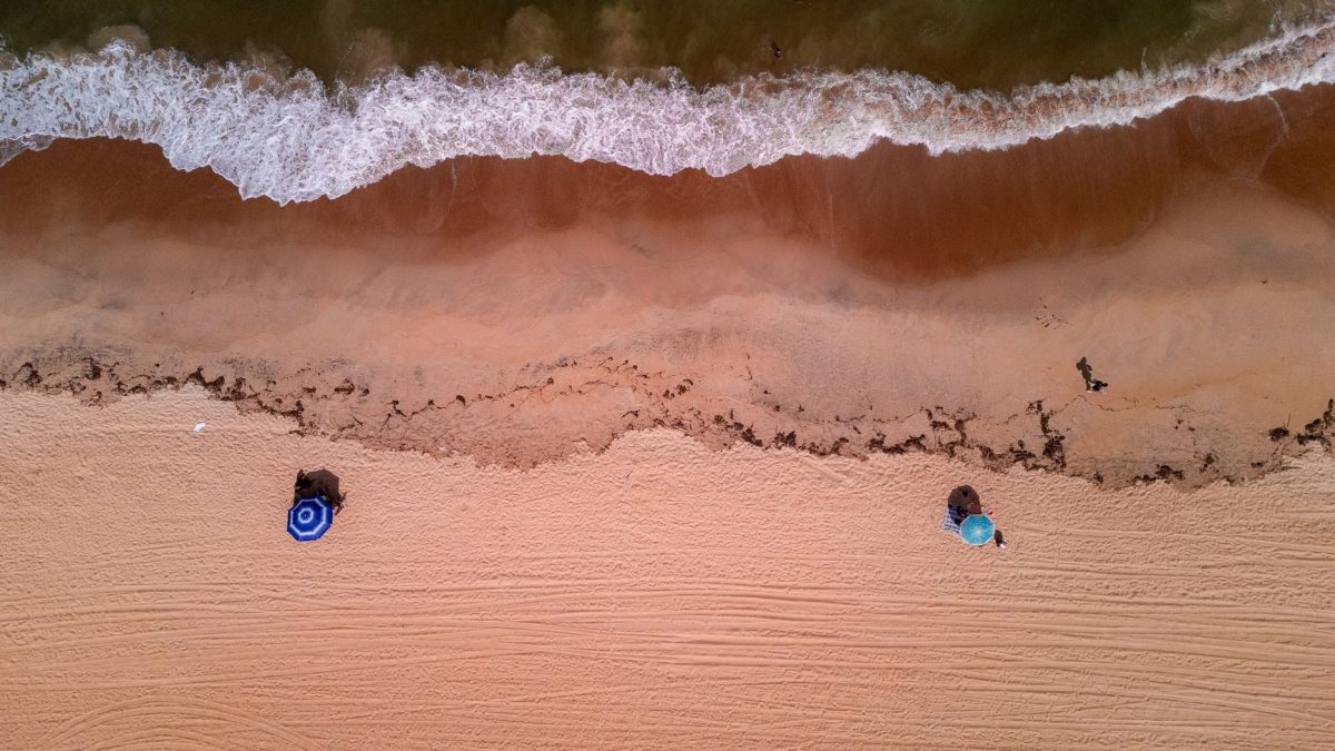 Vista aérea de uma praia brasileira, com ondas avançando sobre a faixa de areia.