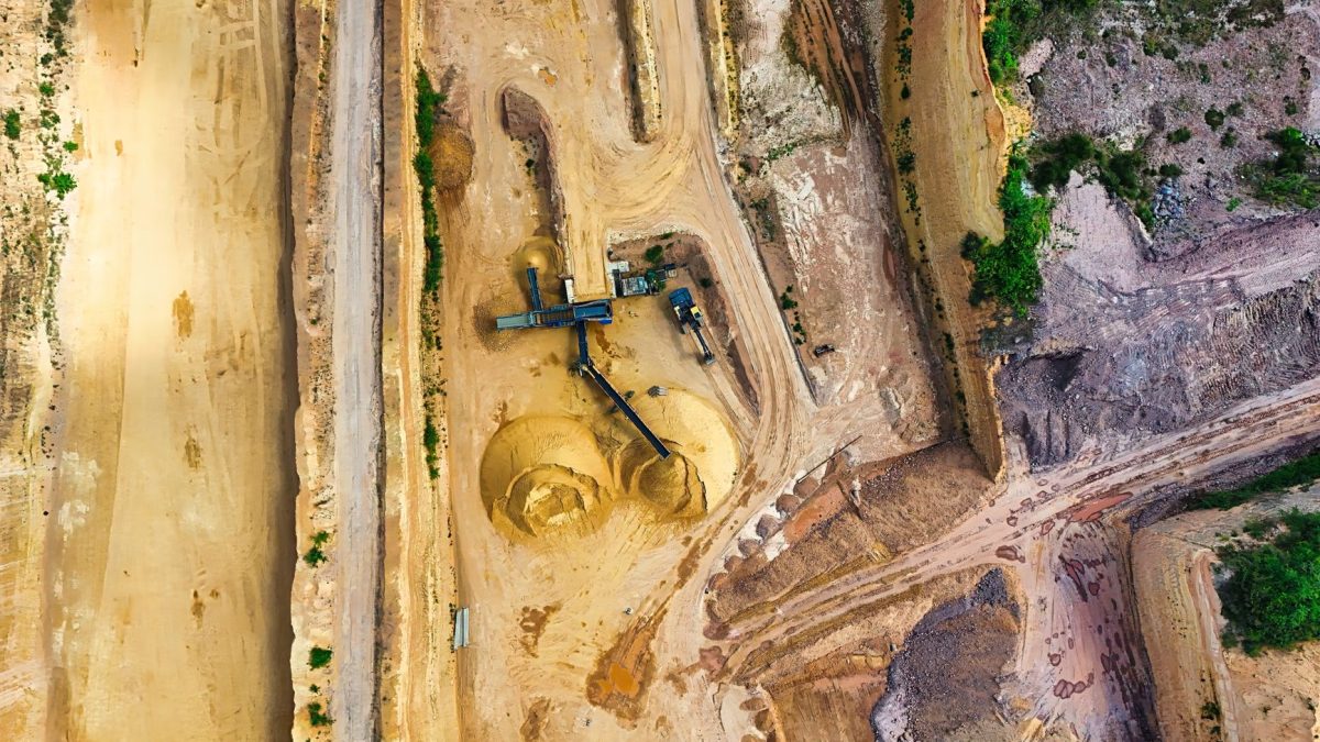 Vista aérea de uma mina a céu aberto, com máquinas industriais e vias de circulação entre as áreas de escavação.