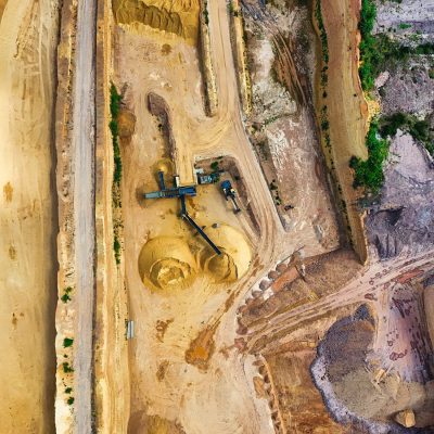 Vista aérea de uma mina a céu aberto, com máquinas industriais e vias de circulação entre as áreas de escavação.