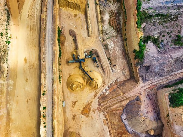 Vista aérea de uma mina a céu aberto, com máquinas industriais e vias de circulação entre as áreas de escavação.