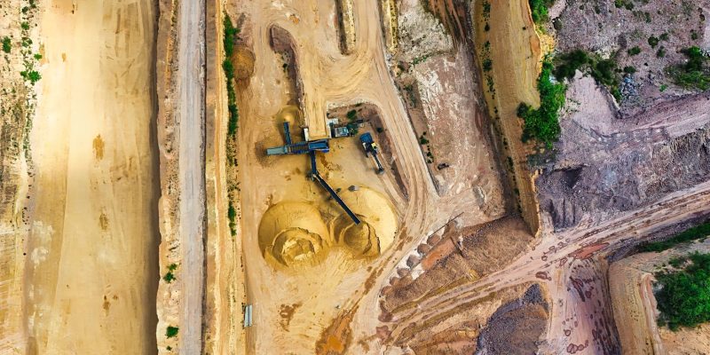 Vista aérea de uma mina a céu aberto, com máquinas industriais e vias de circulação entre as áreas de escavação.