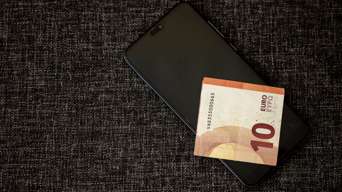 Nota de dez euros sobre um smartphone apoiado em tecido escuro.