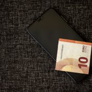 Nota de dez euros sobre um smartphone apoiado em tecido escuro.