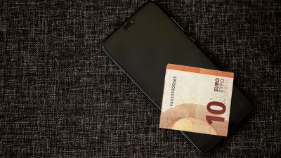 Nota de dez euros sobre um smartphone apoiado em tecido escuro.