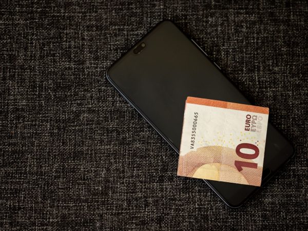 Nota de dez euros sobre um smartphone apoiado em tecido escuro.