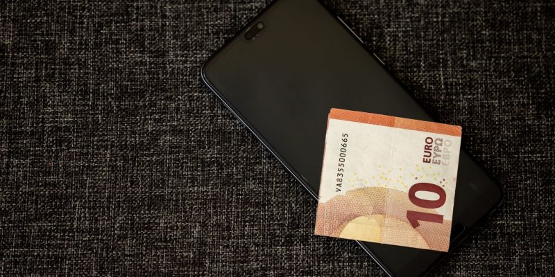 Nota de dez euros sobre um smartphone apoiado em tecido escuro.