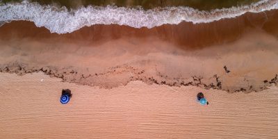 Vista aérea de uma praia brasileira, com ondas avançando sobre a faixa de areia.