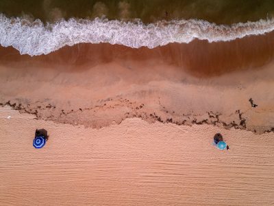 Vista aérea de uma praia brasileira, com ondas avançando sobre a faixa de areia.