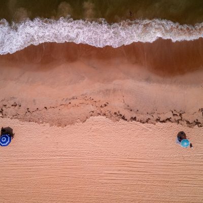 Vista aérea de uma praia brasileira, com ondas avançando sobre a faixa de areia.