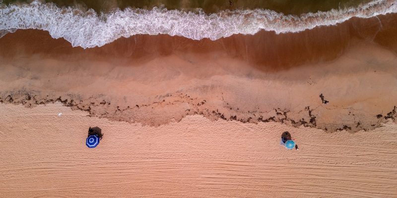 Vista aérea de uma praia brasileira, com ondas avançando sobre a faixa de areia.