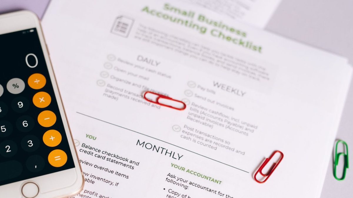 Checklist e calculadora sobre uma mesa, representando o controle financeiro de um pequeno negócio.