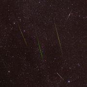 Meteoros luminosos cruzam um céu noturno repleto de estrelas durante uma chuva de meteoros.