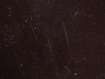 Meteoros luminosos cruzam um céu noturno repleto de estrelas durante uma chuva de meteoros.