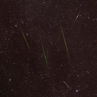 Meteoros luminosos cruzam um céu noturno repleto de estrelas durante uma chuva de meteoros.