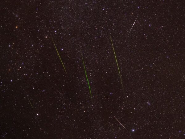 Meteoros luminosos cruzam um céu noturno repleto de estrelas durante uma chuva de meteoros.
