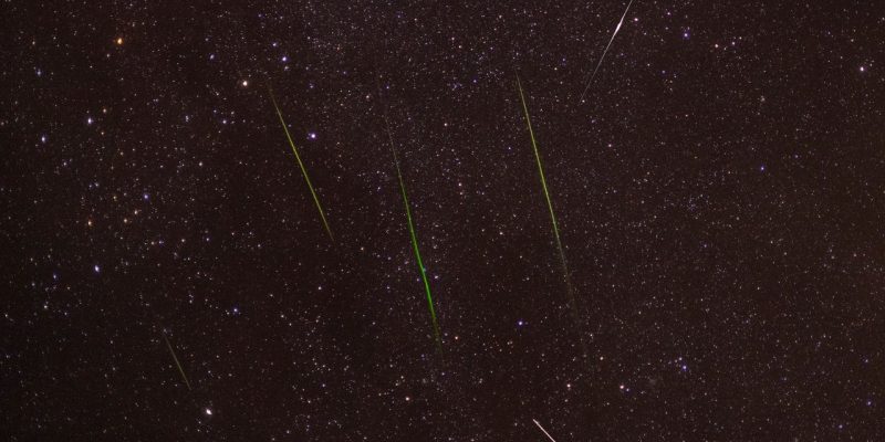 Meteoros luminosos cruzam um céu noturno repleto de estrelas durante uma chuva de meteoros.