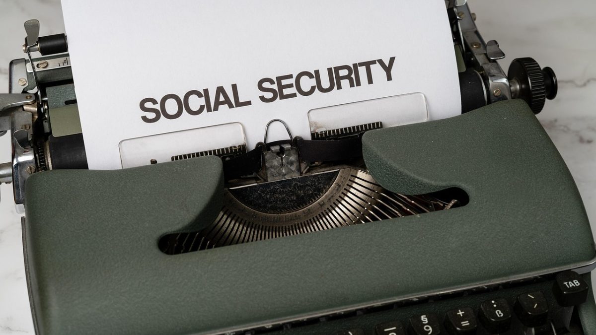 Máquina de escrever com referência à seguridade social, acompanhada de elementos que remetem a benefícios públicos e apoio econômico.