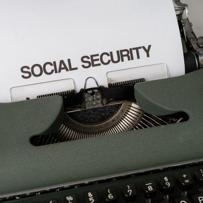 Máquina de escrever com referência à seguridade social, acompanhada de elementos que remetem a benefícios públicos e apoio econômico.