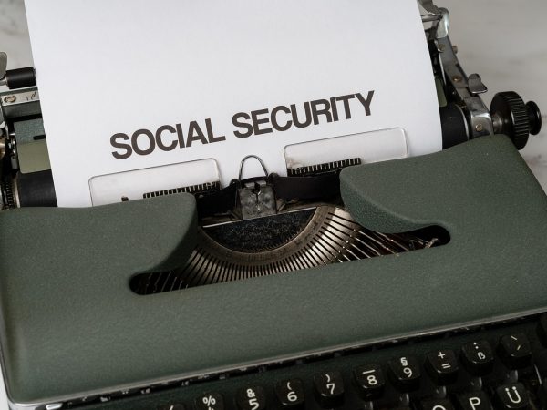 Máquina de escrever com referência à seguridade social, acompanhada de elementos que remetem a benefícios públicos e apoio econômico.
