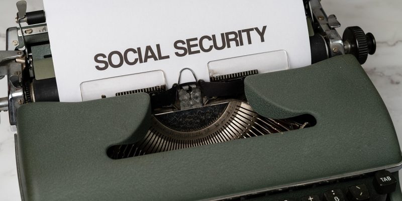 Máquina de escrever com referência à seguridade social, acompanhada de elementos que remetem a benefícios públicos e apoio econômico.